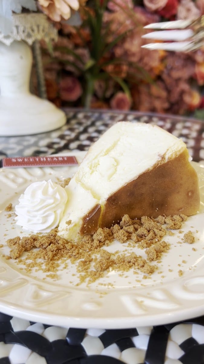 A slice of baked cheesecake with whipped cream and biscuit crumbs