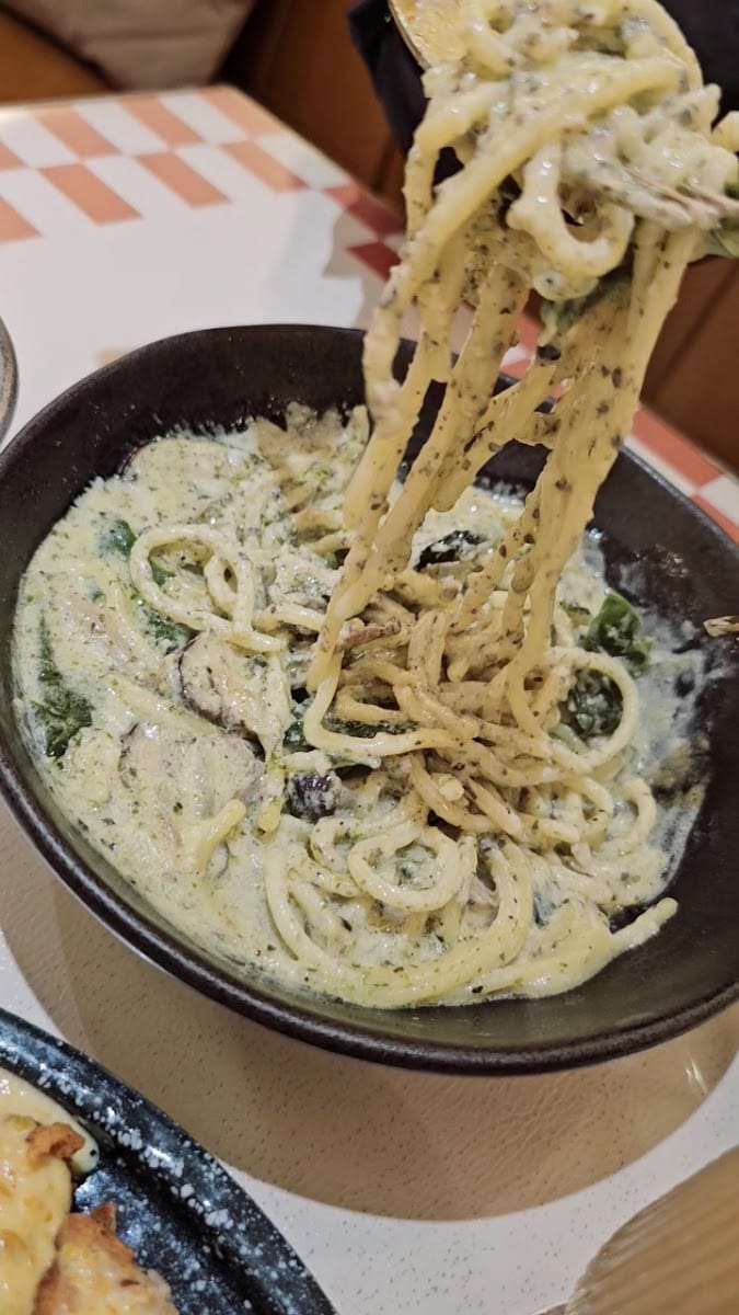 Creamy herb pasta in a black bowl, lifted on a fork