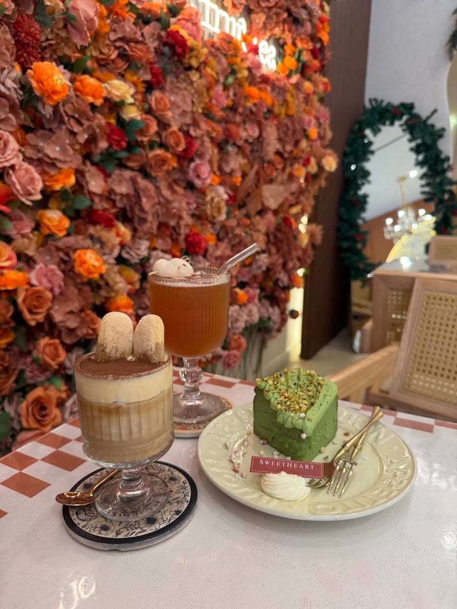 A tiramisu cup, an iced tea and a green-topped cake in front of the flower wall